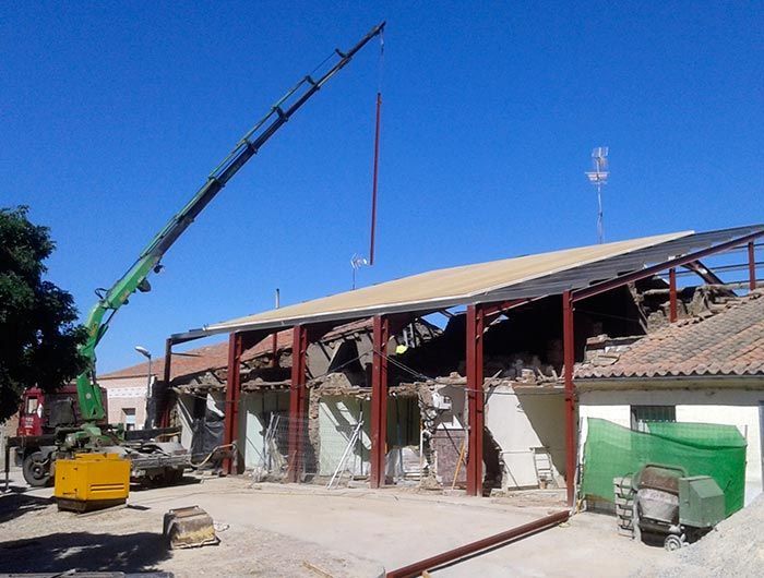Una grúa verde está levantando un techo sobre un edificio.