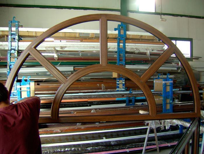 Un hombre con una camisa roja está parado frente a una gran ventana de madera.