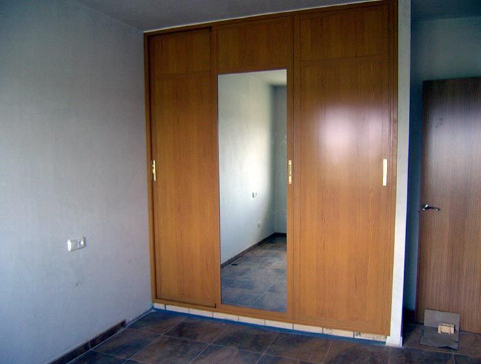 Una habitación vacía con un armario de madera y un espejo.