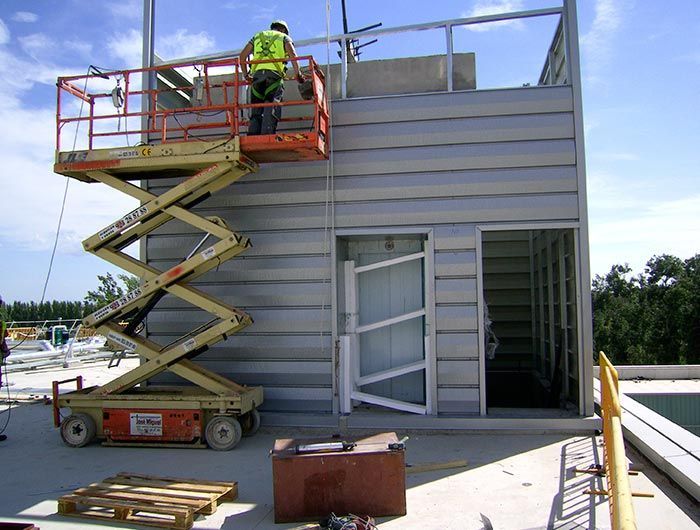 Un hombre en un elevador de tijera está trabajando en un edificio.