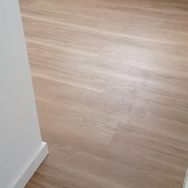 Un primer plano de un piso de madera en una habitación con una pared blanca.
