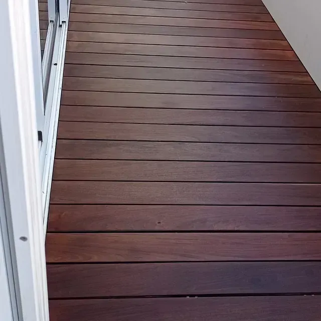 Una terraza de madera con una puerta corrediza de vidrio al fondo.