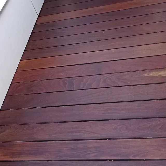 Un primer plano de una terraza de madera con una pared blanca al fondo.