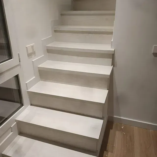 Un conjunto de escaleras blancas en una habitación al lado de una ventana.