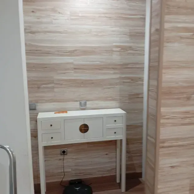 Un escritorio blanco con cajones está frente a una pared de madera.