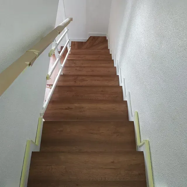 Una escalera de madera con barandilla blanca que sube al segundo piso de una casa.
