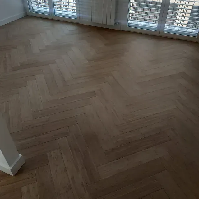 Un suelo de madera con diseño de espiga en una habitación con muchas ventanas.
