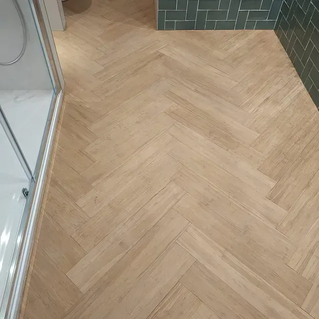 Un baño con suelo de madera y azulejos verdes.