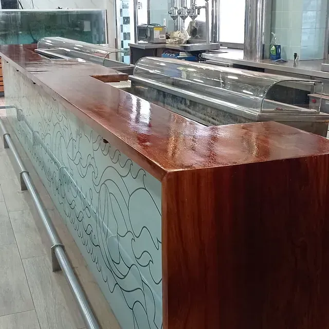 Un largo mostrador de madera en un restaurante con una encimera de vidrio.