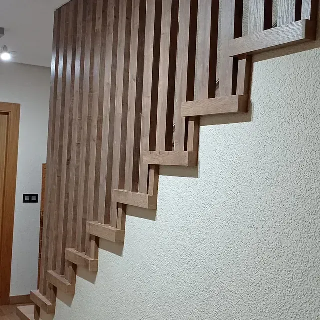 Una escalera de madera con una barandilla de madera contra una pared blanca.