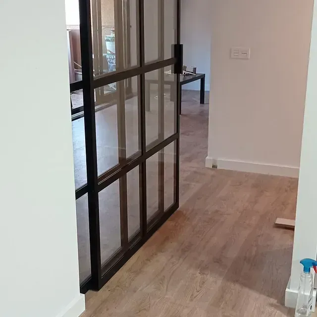 Un pasillo con una puerta corrediza de vidrio entre dos habitaciones.