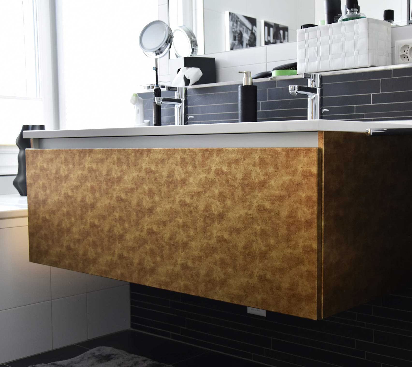 Meuble-lavabo suspendu à texture dorée dans une salle de bains avec carrelage noir.