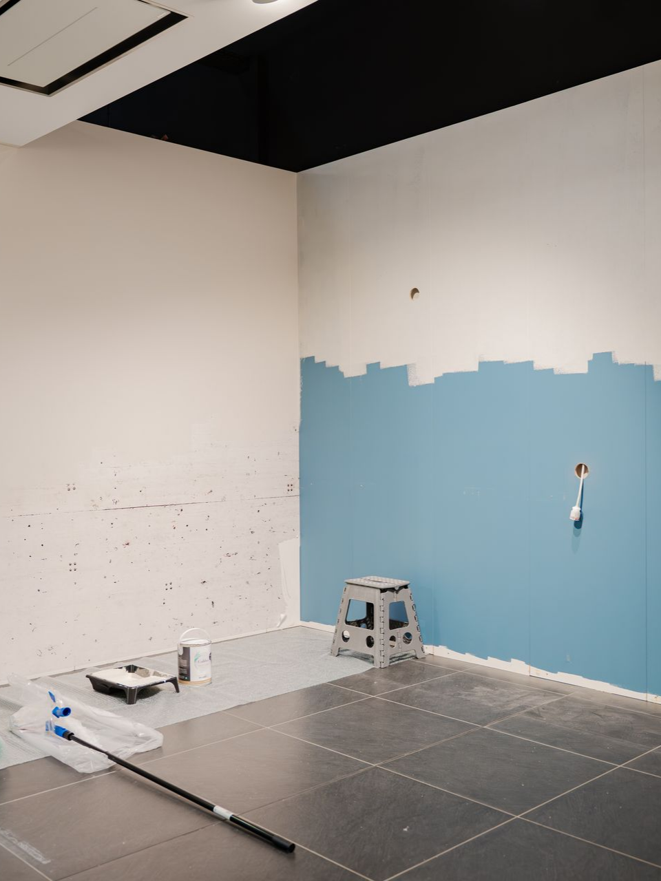Pièce aux murs peints en bleu et blanc, avec un tabouret et du matériel de peinture éparpillé sur le sol.