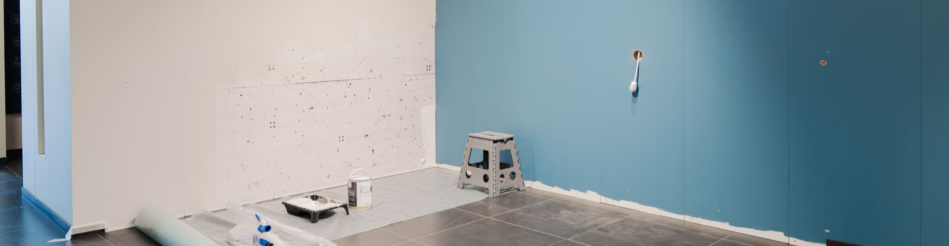 Une pièce aux murs blancs et bleus, avec un petit escabeau et des outils posés au sol.