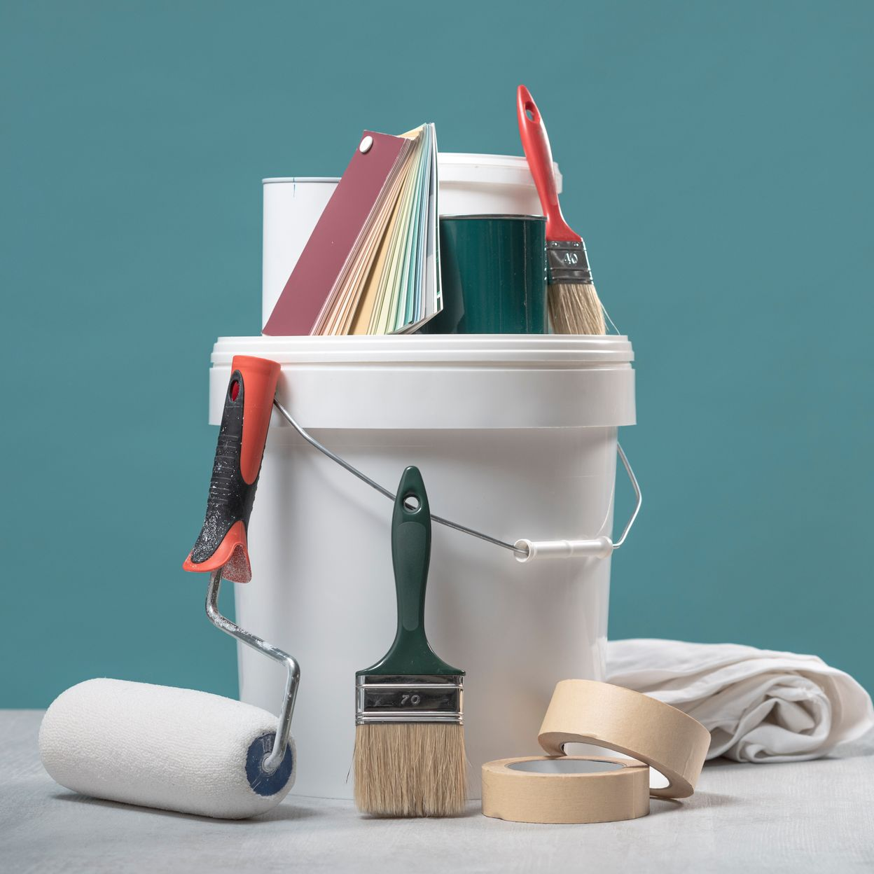 Matériel de peinture : seau, pinceaux, rouleau, ruban adhésif, échantillons de couleurs sur fond turquoise.