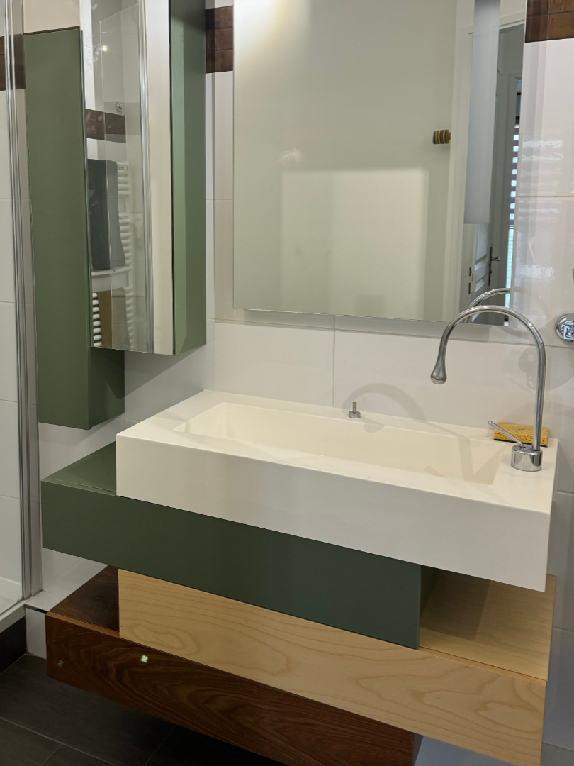 Salle de bains moderne avec lavabo blanc, grand miroir et rangements en bois beige et vert.