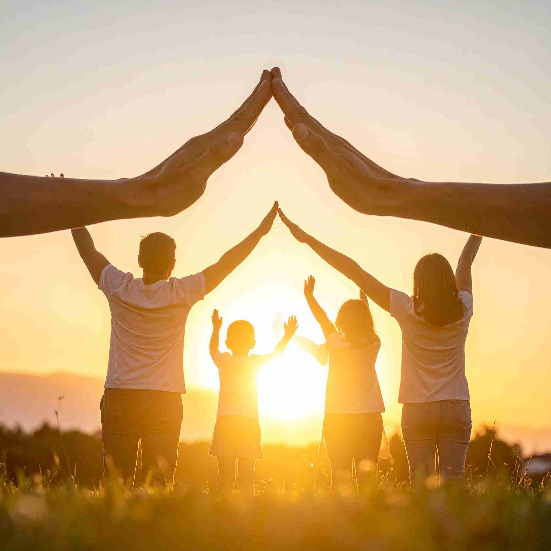 Una familia forma una casa con sus cuerpos y manos al atardecer.