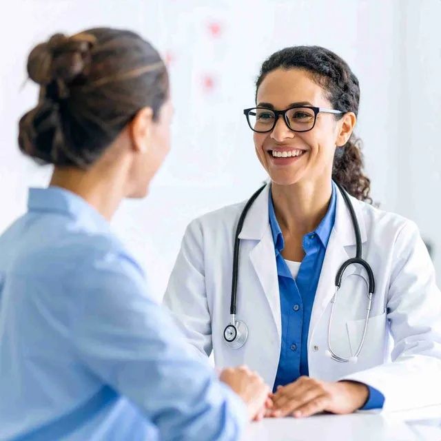 Un médico con bata blanca y gafas sonríe a un paciente en un consultorio médico.