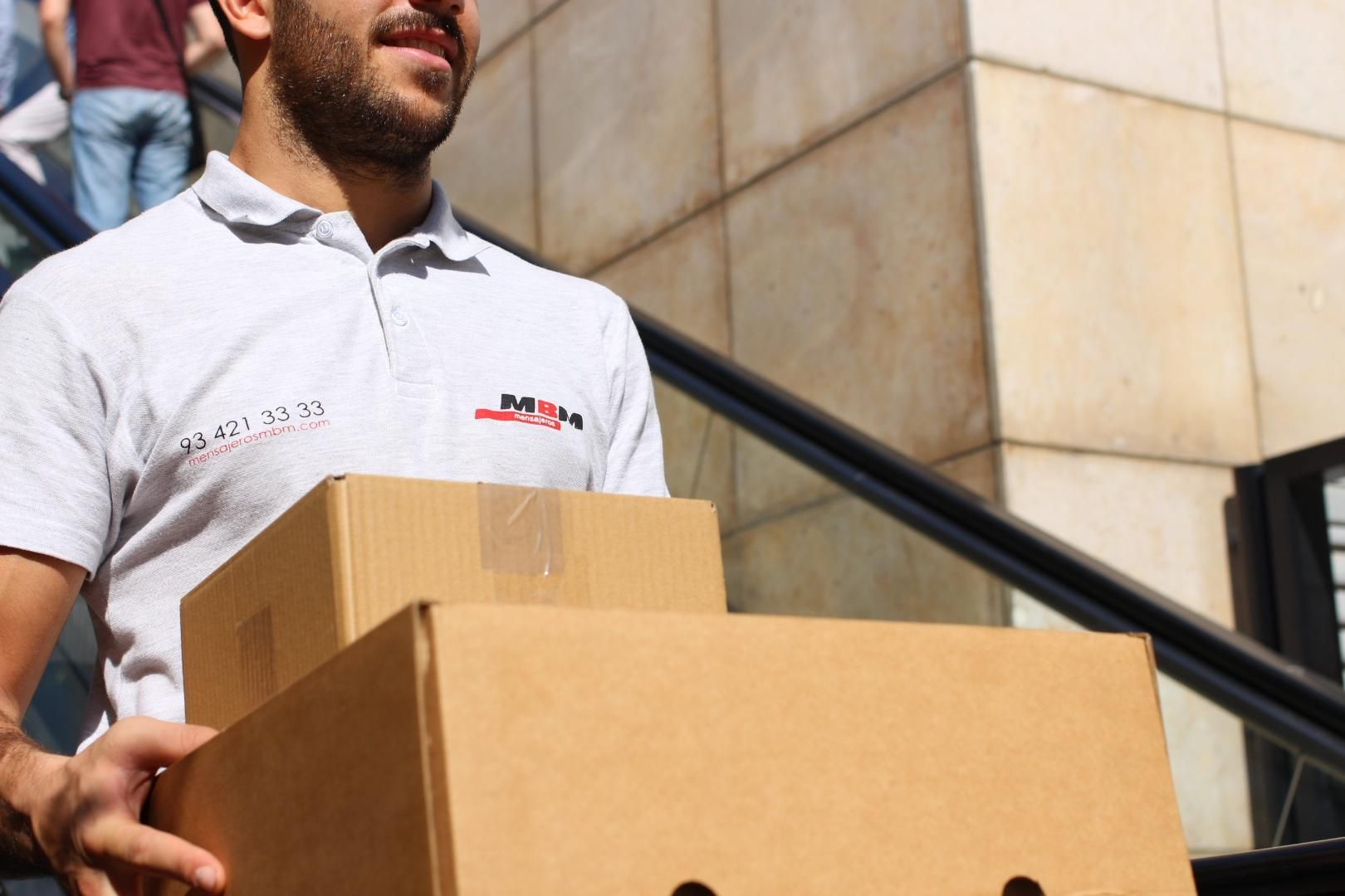 Un hombre con una camisa blanca lleva una pila de cajas de cartón.
