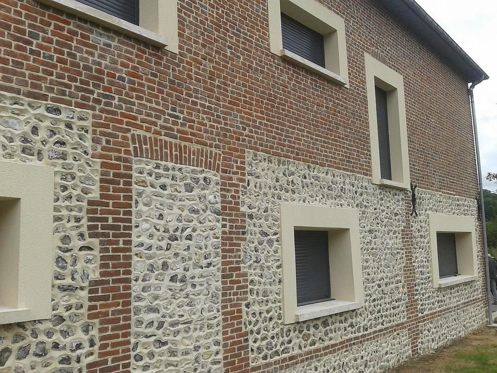 Mur extérieur d'un bâtiment présentant un mélange de briques rouges à motifs, de pierres de silex claires et de fenêtres modernes.
