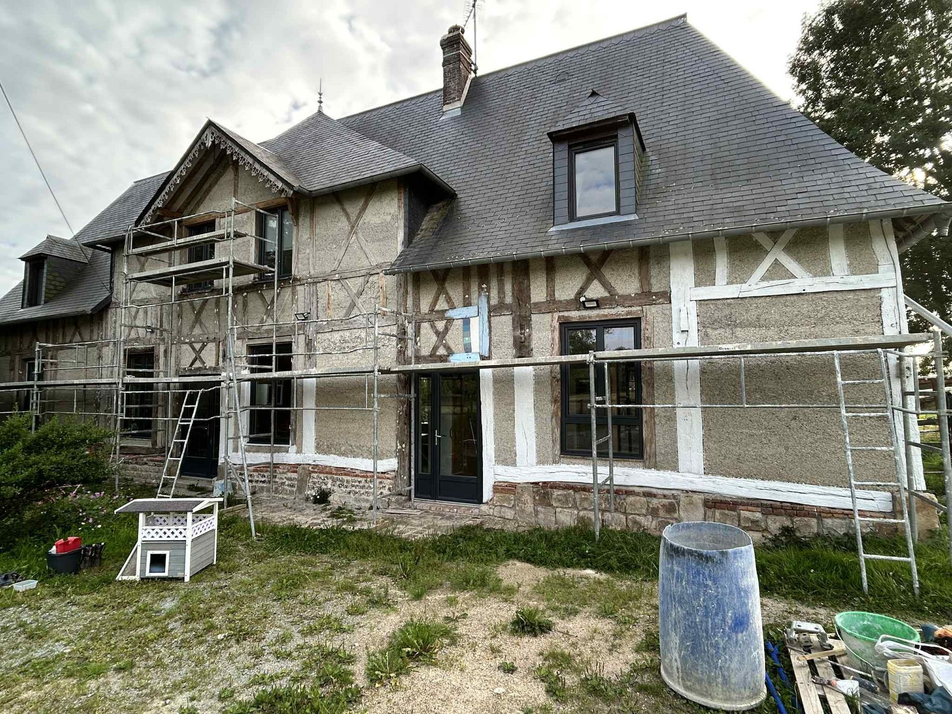 Une maison à colombages de deux étages en cours de rénovation, avec des échafaudages installés sur sa façade extérieure.