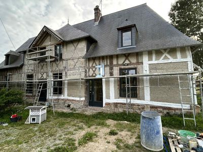 Une maison à ossature bois de deux étages en cours de rénovation extérieure, avec des échafaudages entourant la façade et le toit.