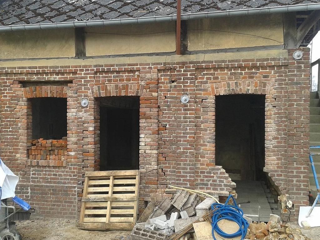 Un vieux bâtiment en briques en cours de rénovation, avec deux portes ouvertes et une fenêtre obstruée par des briques descellées.