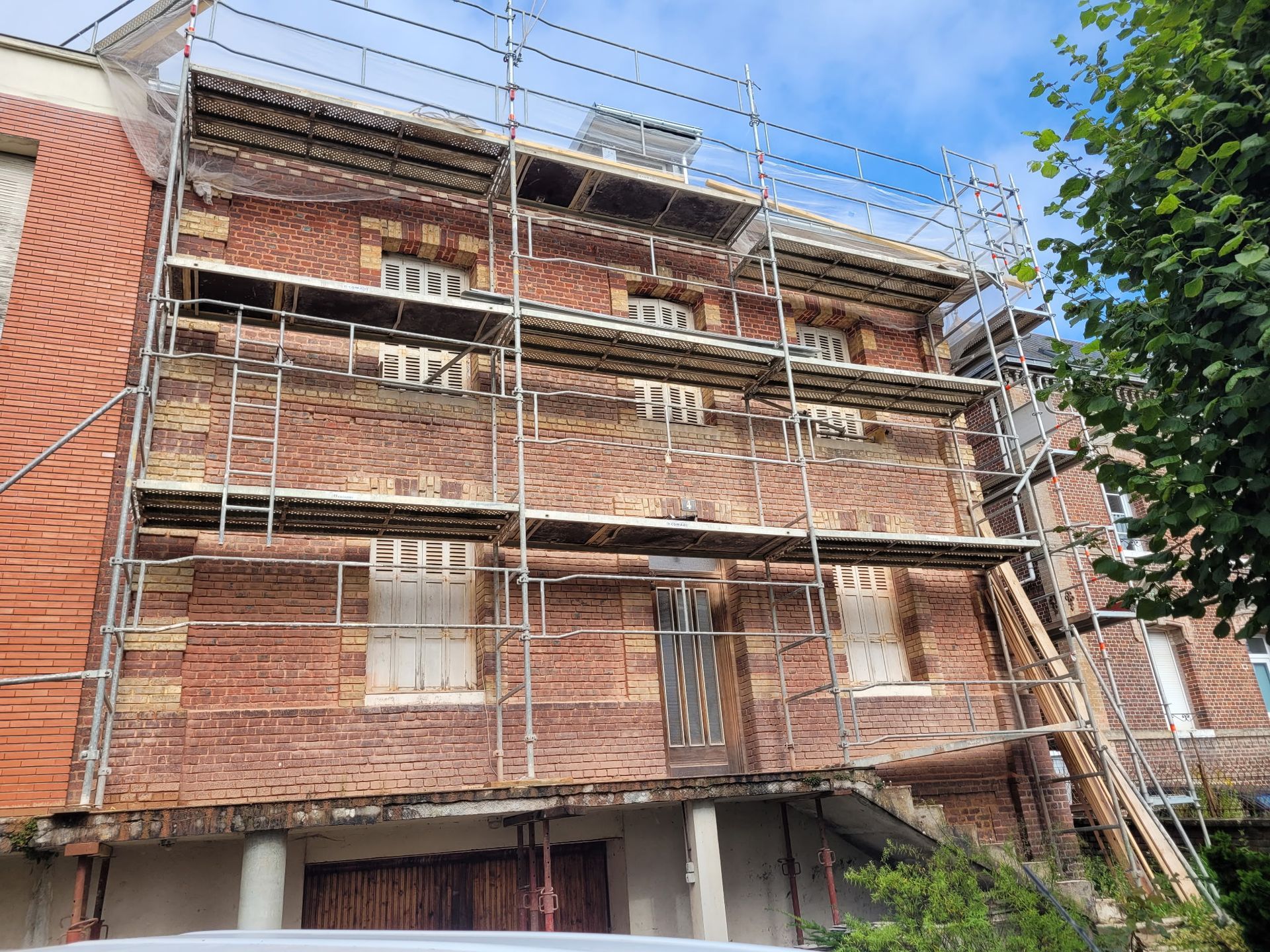 Un bâtiment de trois étages en briques rouges en cours de rénovation, avec des échafaudages métalliques recouvrant sa façade.