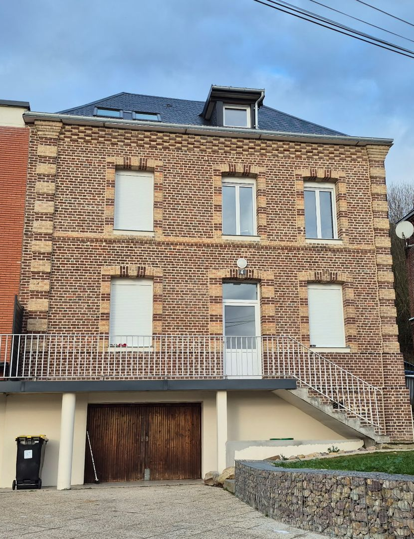 Une maison de trois étages avec une façade caractéristique en briques et en pierres à rayures, un garage au niveau inférieur et un balcon.