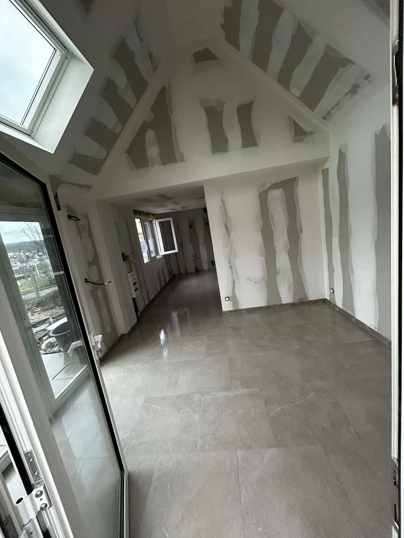 Une pièce en construction, inachevée, avec des plafonds voûtés, un sol carrelé gris et des joints de cloisons sèches apparents.