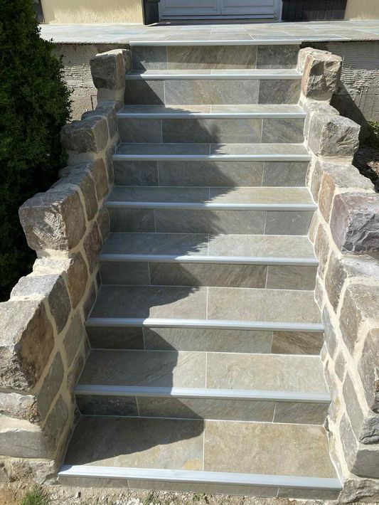 Un escalier en pierre menant à l'entrée d'un bâtiment, doté de marches en pierre grise avec des bandes antidérapantes de couleur claire.