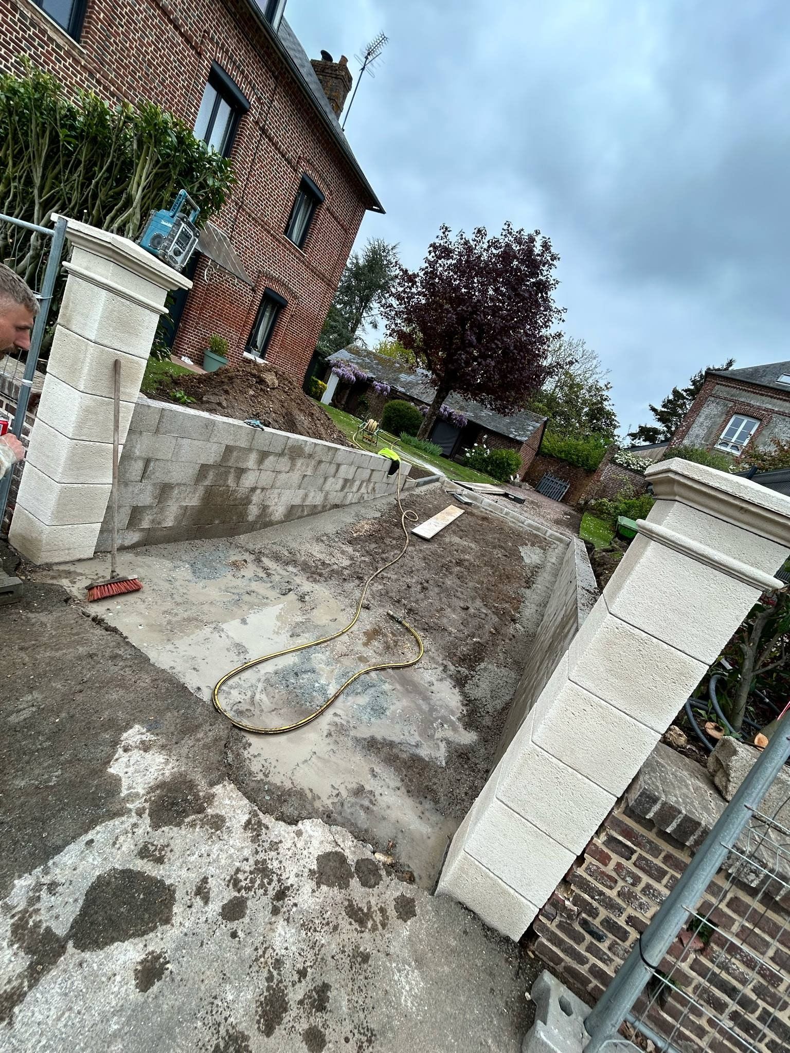 Une entrée résidentielle en construction, caractérisée par deux hauts piliers en pierre claire encadrant une allée de gravier.
