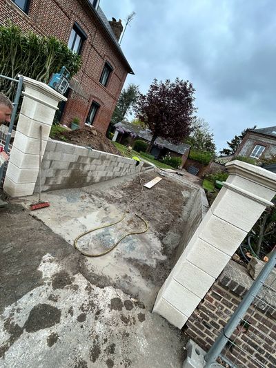 Un chantier de construction montrant deux nouveaux piliers de portail en pierre de part et d'autre d'une allée devant une maison en briques.