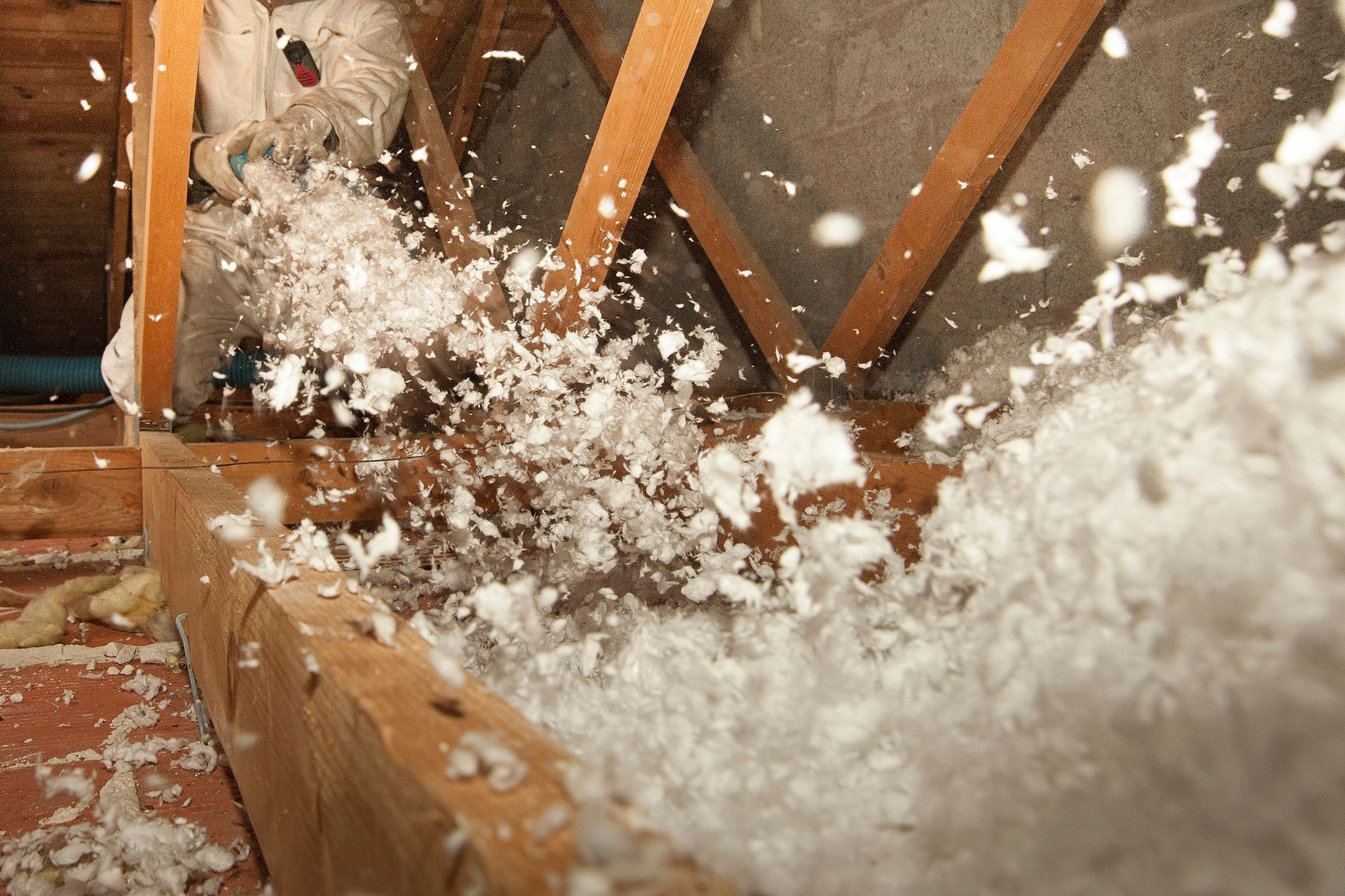 Une personne portant un équipement de protection pulvérise de l'isolant blanc soufflé entre les solives en bois du grenier.