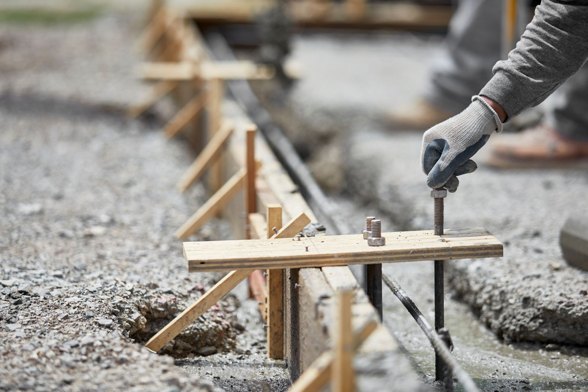 Une personne portant des gants de travail ajuste un piquet d'armature métallique inséré dans un coffrage en bois pour une fondation en béton.