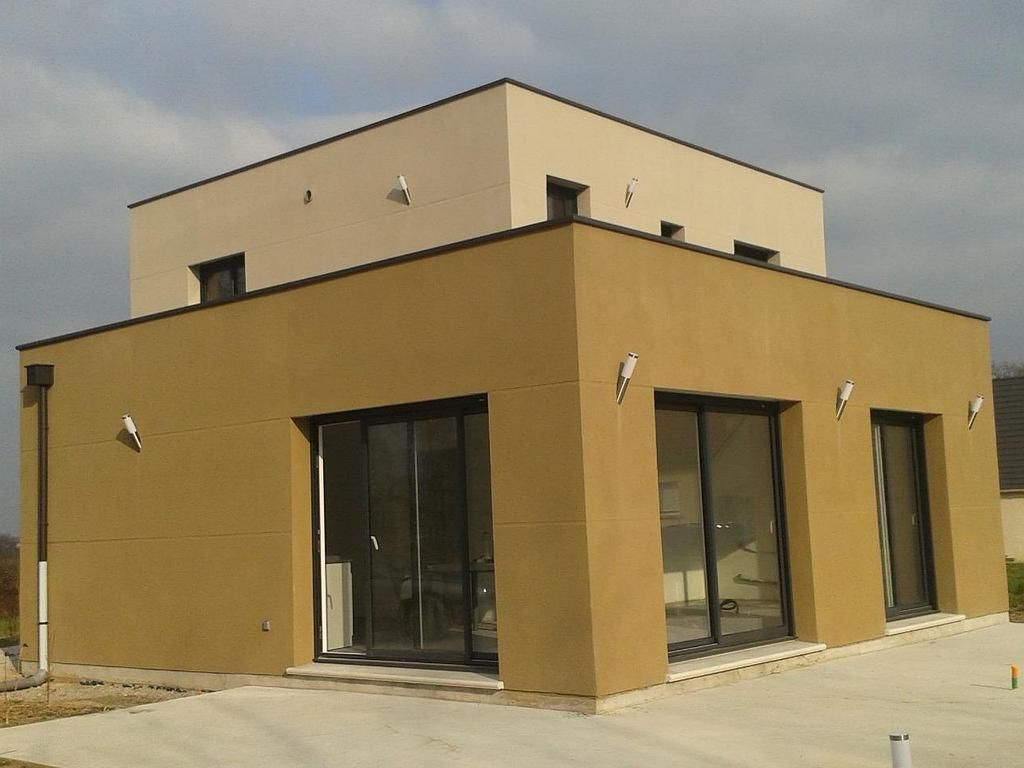 Une maison moderne à deux étages, avec un rez-de-chaussée couleur beige et un étage supérieur couleur crème plus clair, sous un ciel nuageux.