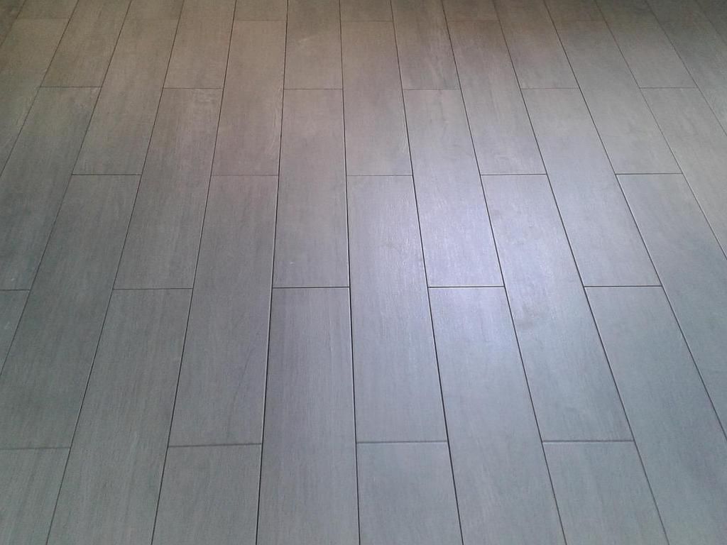 Un sol recouvert de lames rectangulaires gris clair imitation bois, disposées en quinconce avec de fins joints foncés.