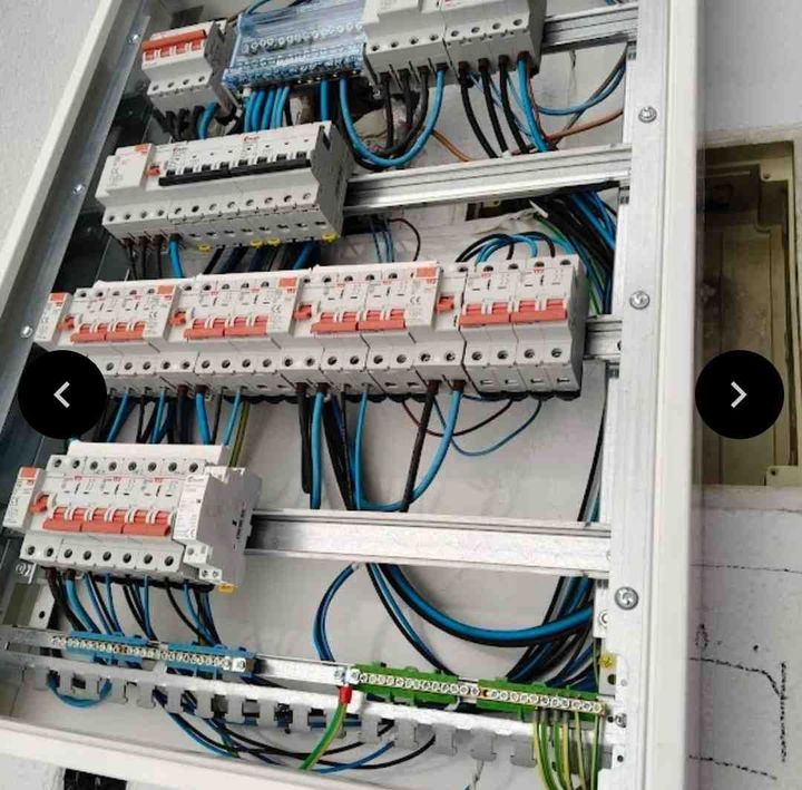 Electricista probando el cableado de un panel eléctrico con un multímetro y unos alicates.