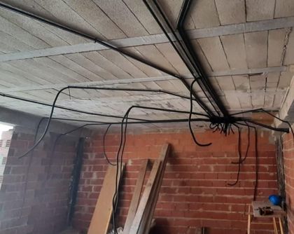 Electricista inspeccionando un panel de pared con un multímetro en una habitación luminosa.