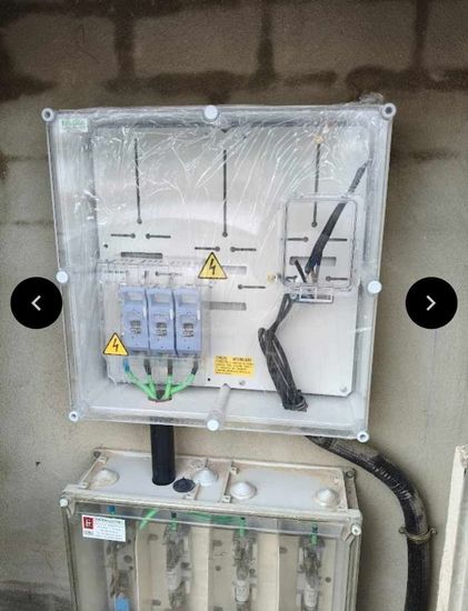 Electricista cableando un panel de disyuntores en una habitación luminosa, con casco y guantes.