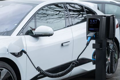 Carga de un coche eléctrico blanco en una estación con cables en espiral al aire libre.