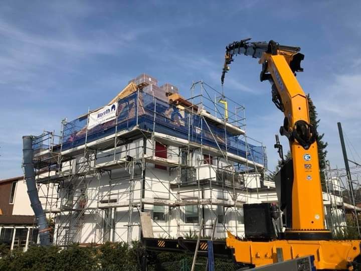 Auf einer Baustelle wird ein Haus mit Gerüste und einem Kran gebaut