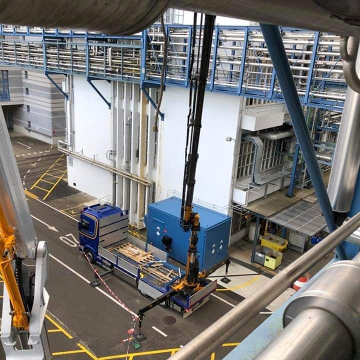 ein blauer Lkw mit einem gelben Kran steht vor einem großen Gebäude