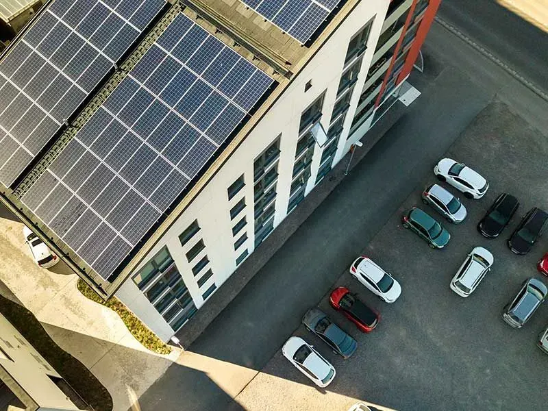 Edificio con paneles solares en el tejado, coches aparcados en el aparcamiento contiguo.