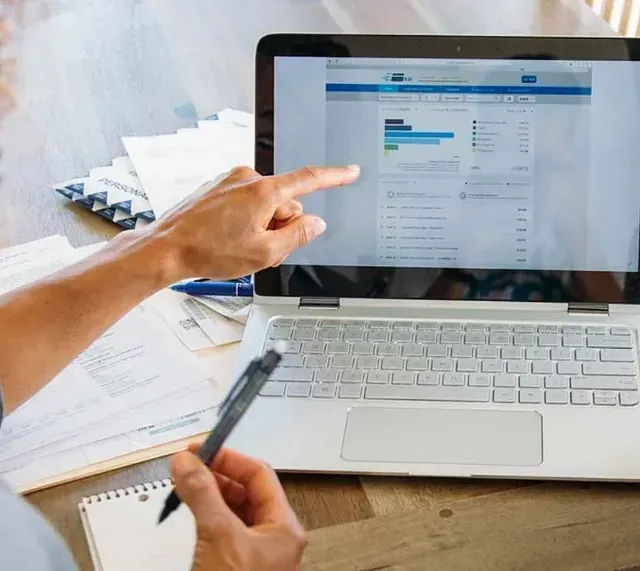 Una persona señala la pantalla de un portátil con gráficos de datos. Un bolígrafo y una libreta están cerca