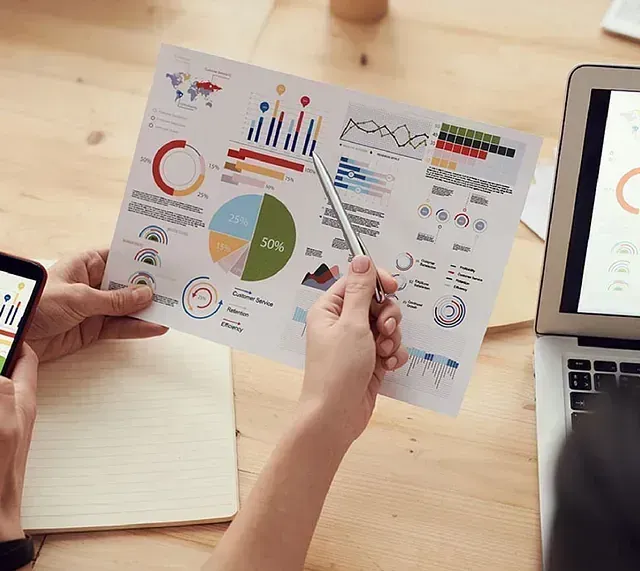 Persona que señala una hoja de datos con tablas y gráficos, y que discute los resultados con un colega.