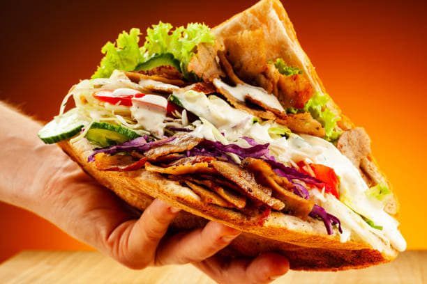 Una persona sostiene un sándwich de kebab en su mano.