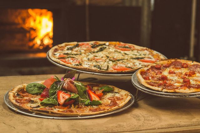 Tres pizzas están sentadas en una mesa de madera frente a un horno.
