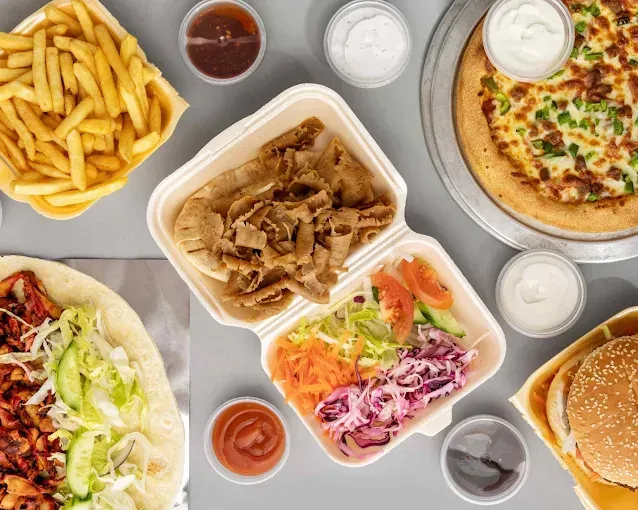 Una mesa cubierta con una variedad de alimentos que incluyen pizza, papas fritas y una hamburguesa.