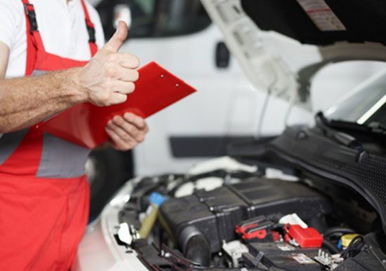 Ein Mann streckt den Daumen nach oben und schaut dabei unter die Motorhaube eines Autos.